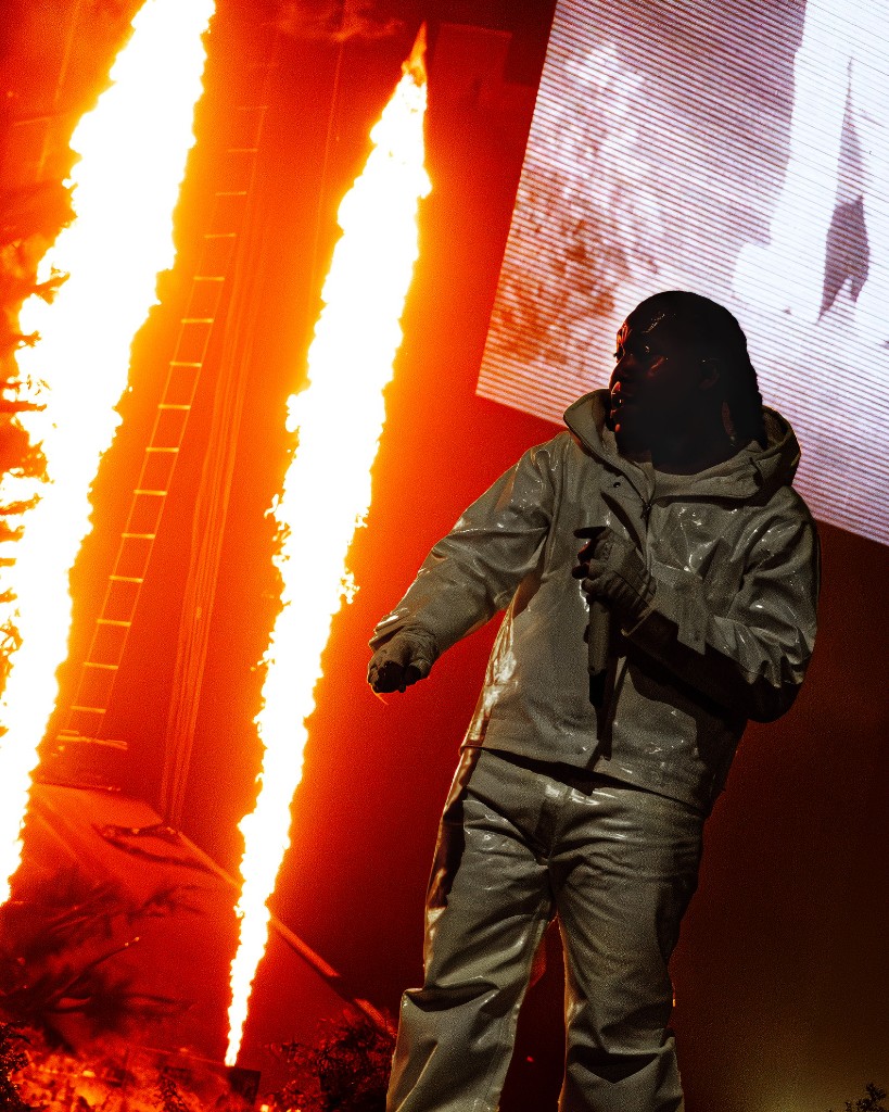 Don Toliver in a reflective white fit as pyrotechnics erupt behind him at the Frost Bank Center.